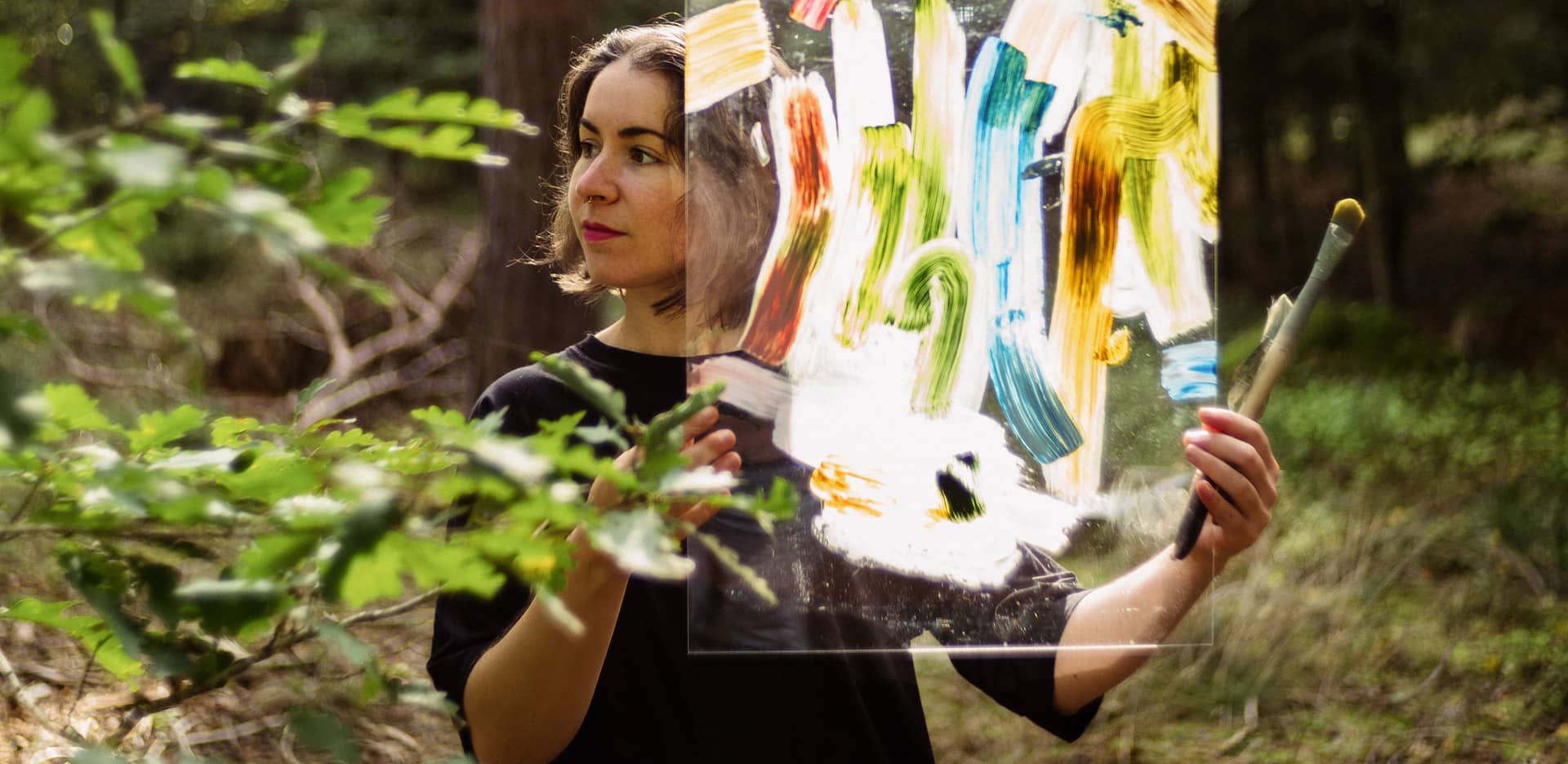 Die Künstlerin Anja Dommel steht mit einem abstrakten Kunstwerk im Sonnenlicht im Wald bei Nürnberg